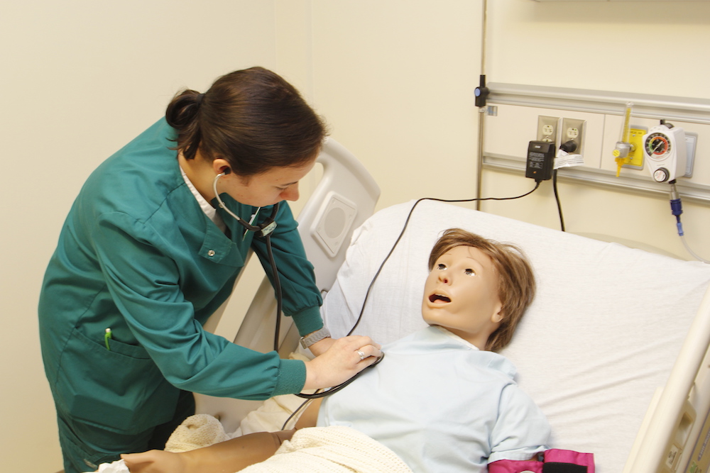 A female nursing student works with an adult patient simulation
